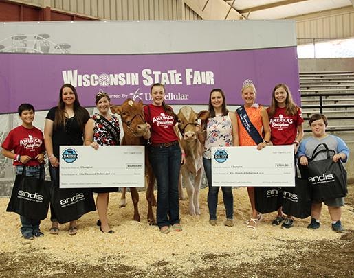 Large version of Six winners, two presenters and two cows standing in front of a Wisconsin State Fair banner at award ceremony with giant novelty checks and Andis tote bags